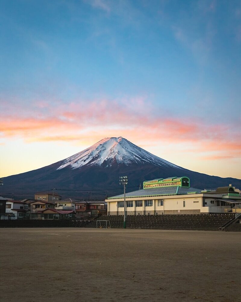 Der schneebedeckte Mount Fuji thront im Abendrot über einem Sportplatz in Fujiyoshida