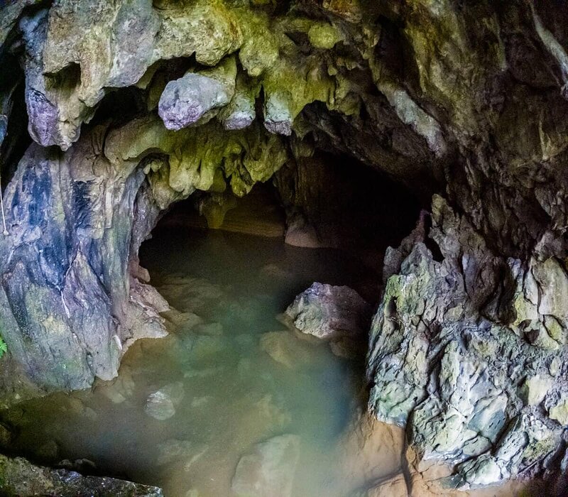 Der Eingang der K'anba-Höhle: Zwischen Felsen schimmert das trübe Höhlenwasser